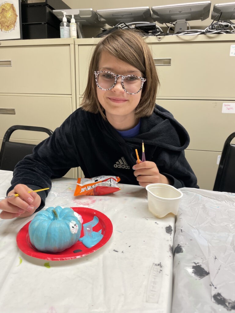 A student painting a small pumpkin at a table