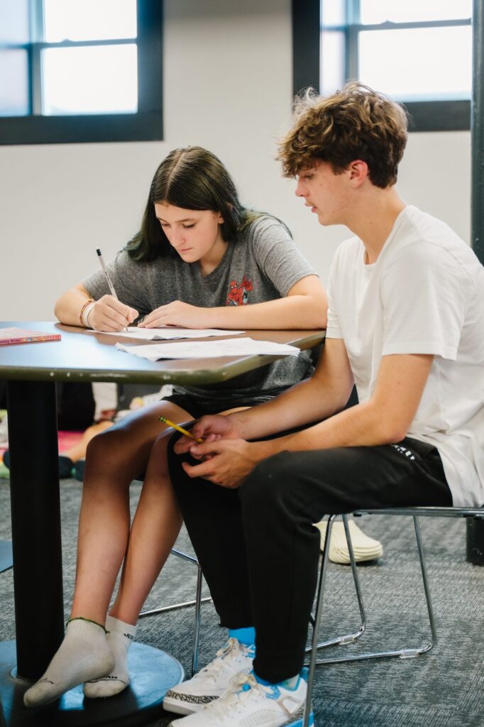 A high school volunteer working through schoolwork beside a younger student