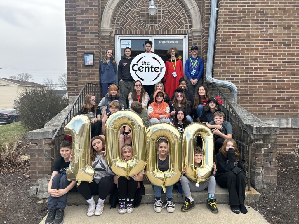 Students holding gold 1000 balloons on The Center's front steps